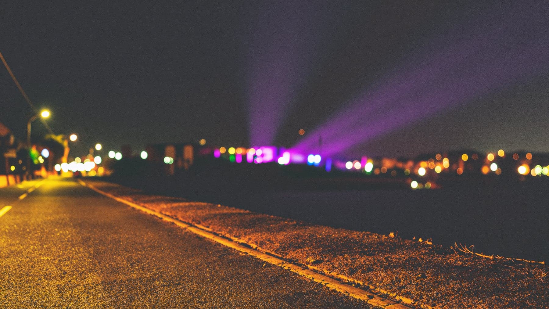 The glow of a club on the horizon at 4am, purple and magenta light spilling into the night over an empty coastal road